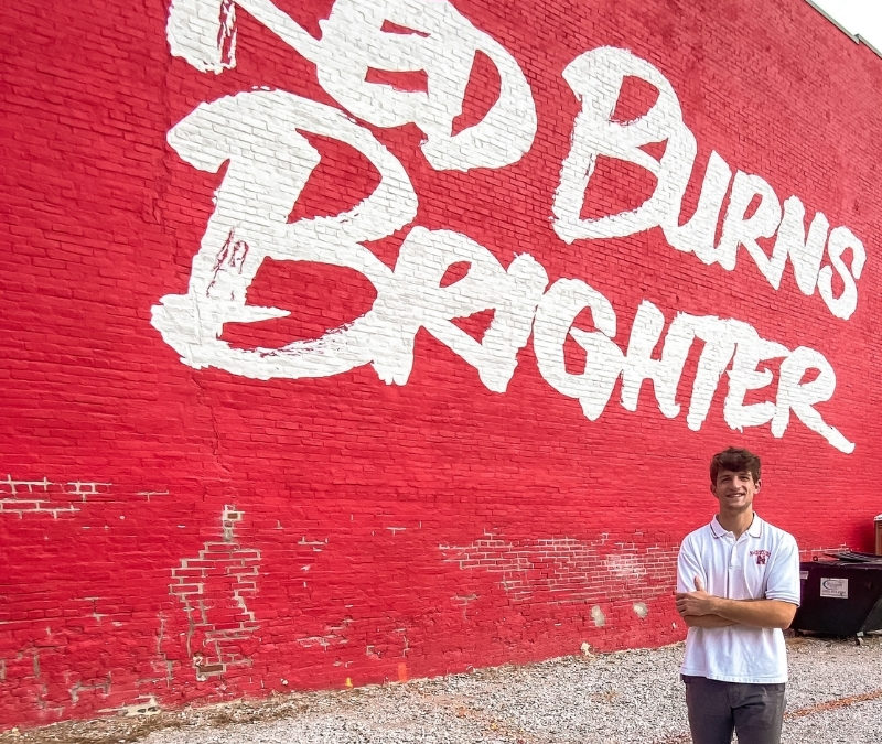 Josh Schrader in front of the Red Burns Brighter mural on Ninth Street going south from downtown Lincoln, Nebraska.